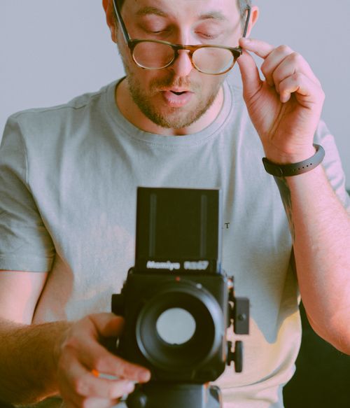 Free Photographer holding a medium format camera while adjusting eyeglasses for a focused shot. Stock Photo