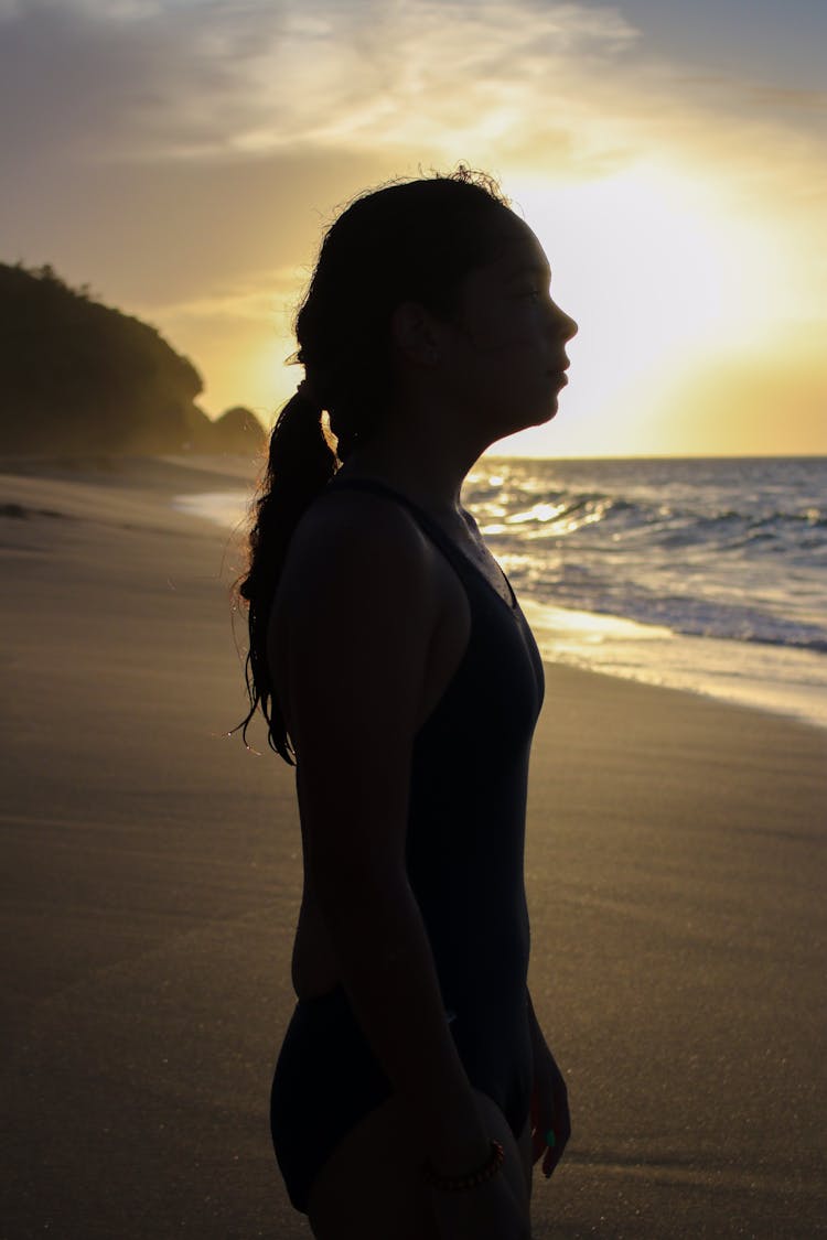 A Silhouette Of A Girl Standing On The Beach During Sunset