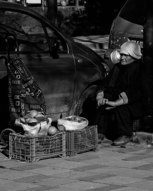 Grayscale Photo of an Elderly Woman Selling Fruits on the Street