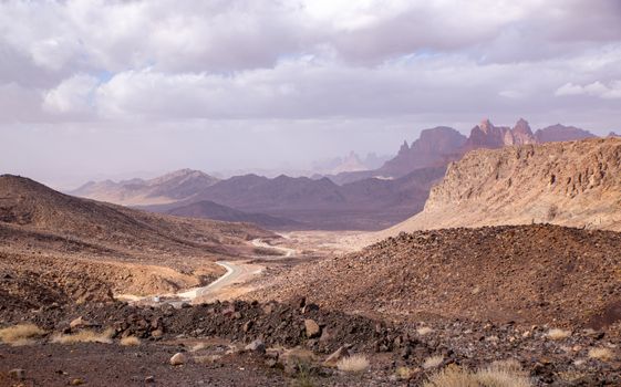 Discover the vast and rugged beauty of a rocky desert with a winding road under a cloudy sky.