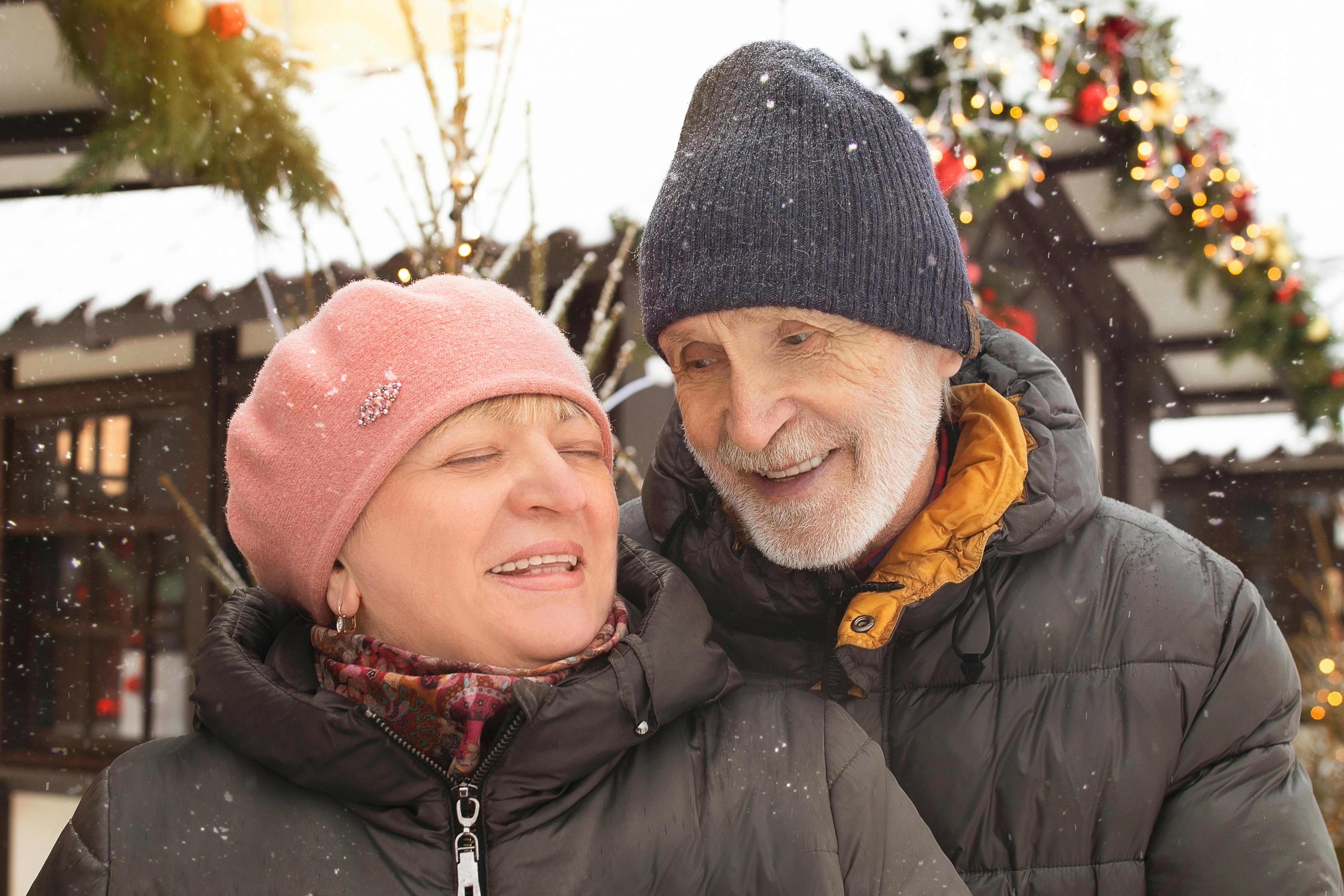 Joyful elderly couple enjoying a snowy winter day outdoors, dressed warmly in winter clothing.