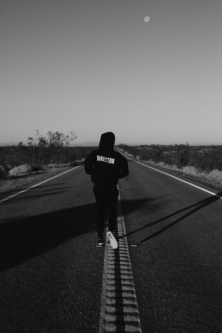 Grayscale Photo Of Man Walking In The Middle Of The Road