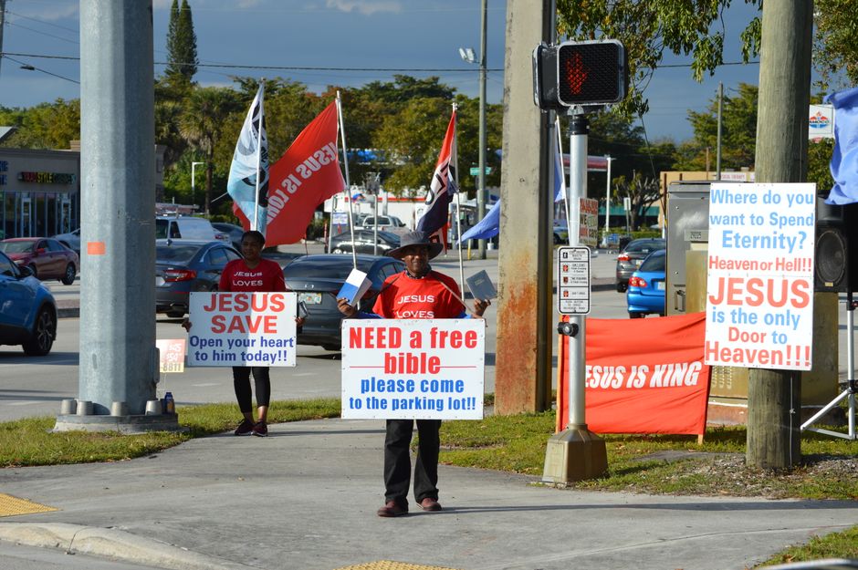 Two individuals holding religious signs on a city sidewalk, conveying Christianity messages.