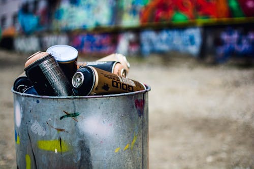 Shabby metal bucket with colorful spray paint placed on street near colorful wall in industrial district