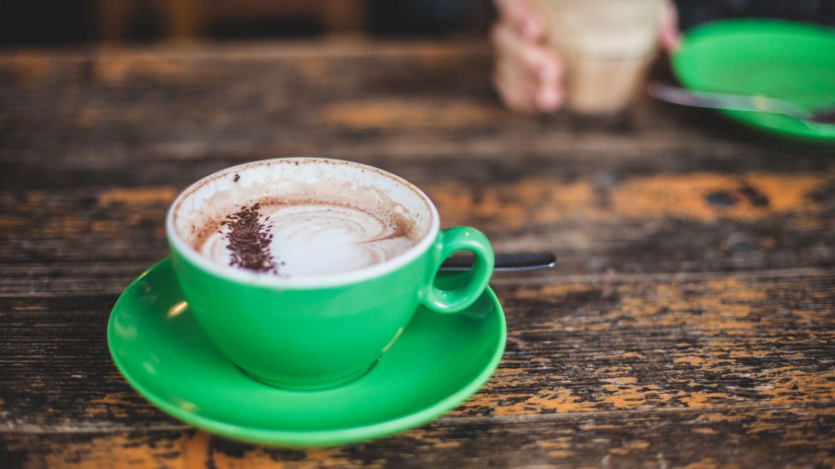 A vibrant green cup of cappuccino on a rustic wooden table with another drink in the background.