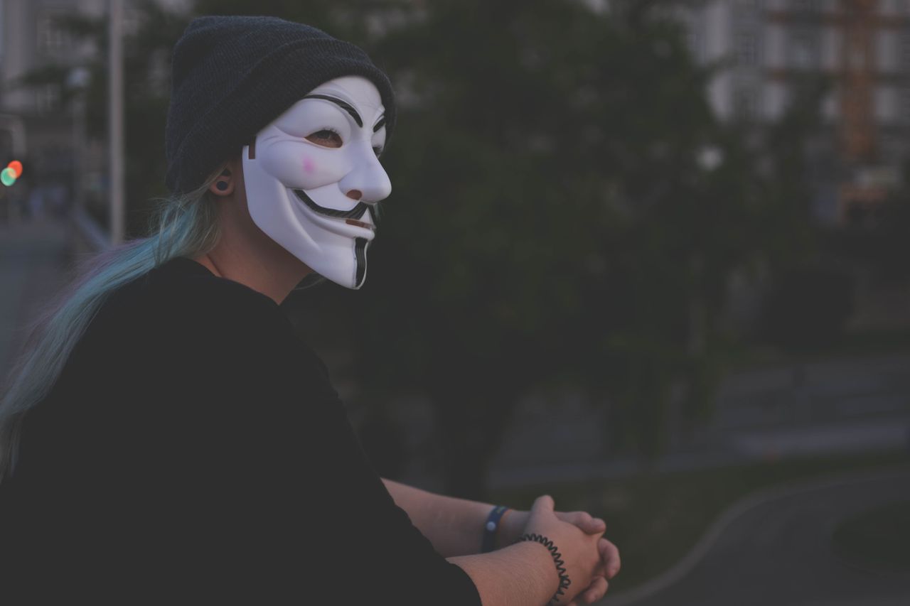 a person wearing a guy fawkes mask stands on a balcony during twilight