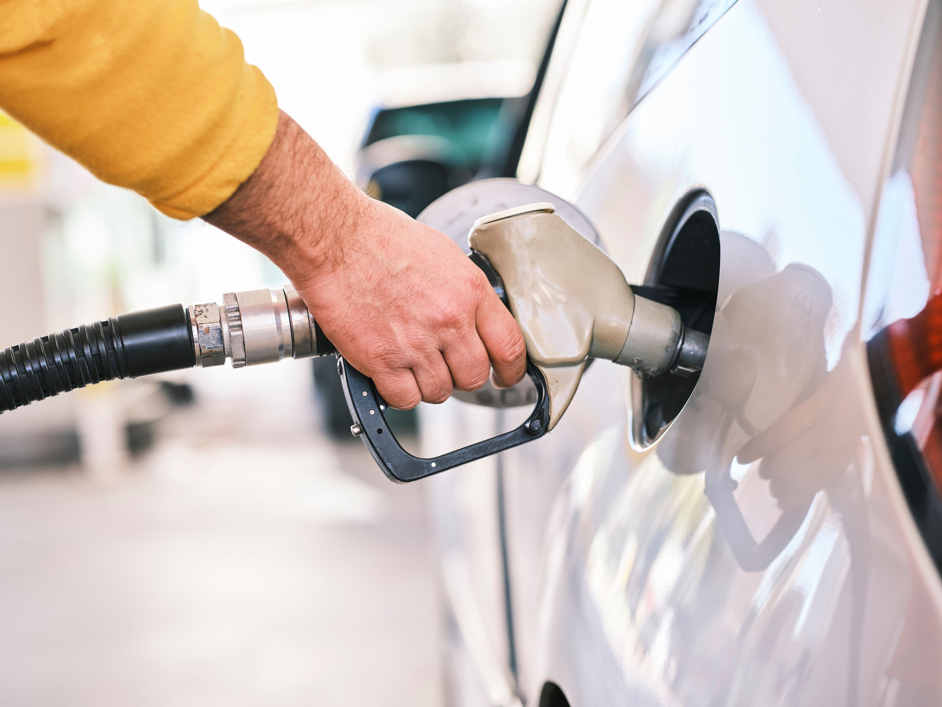 Close-up of a person refueling a car with a gas nozzle at a station.