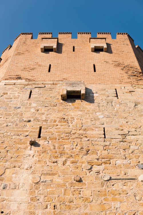 Free Close-up of a medieval castle wall under a clear blue sky, showing architectural details. Stock Photo