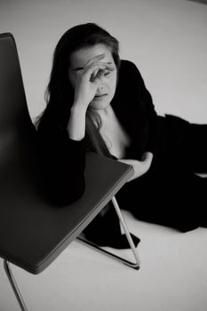 Black and white photo of a woman resting beside a chair in a studio setting.