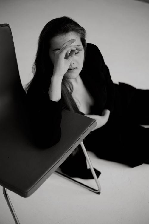 Free Black and white photo of a woman resting beside a chair in a studio setting. Stock Photo