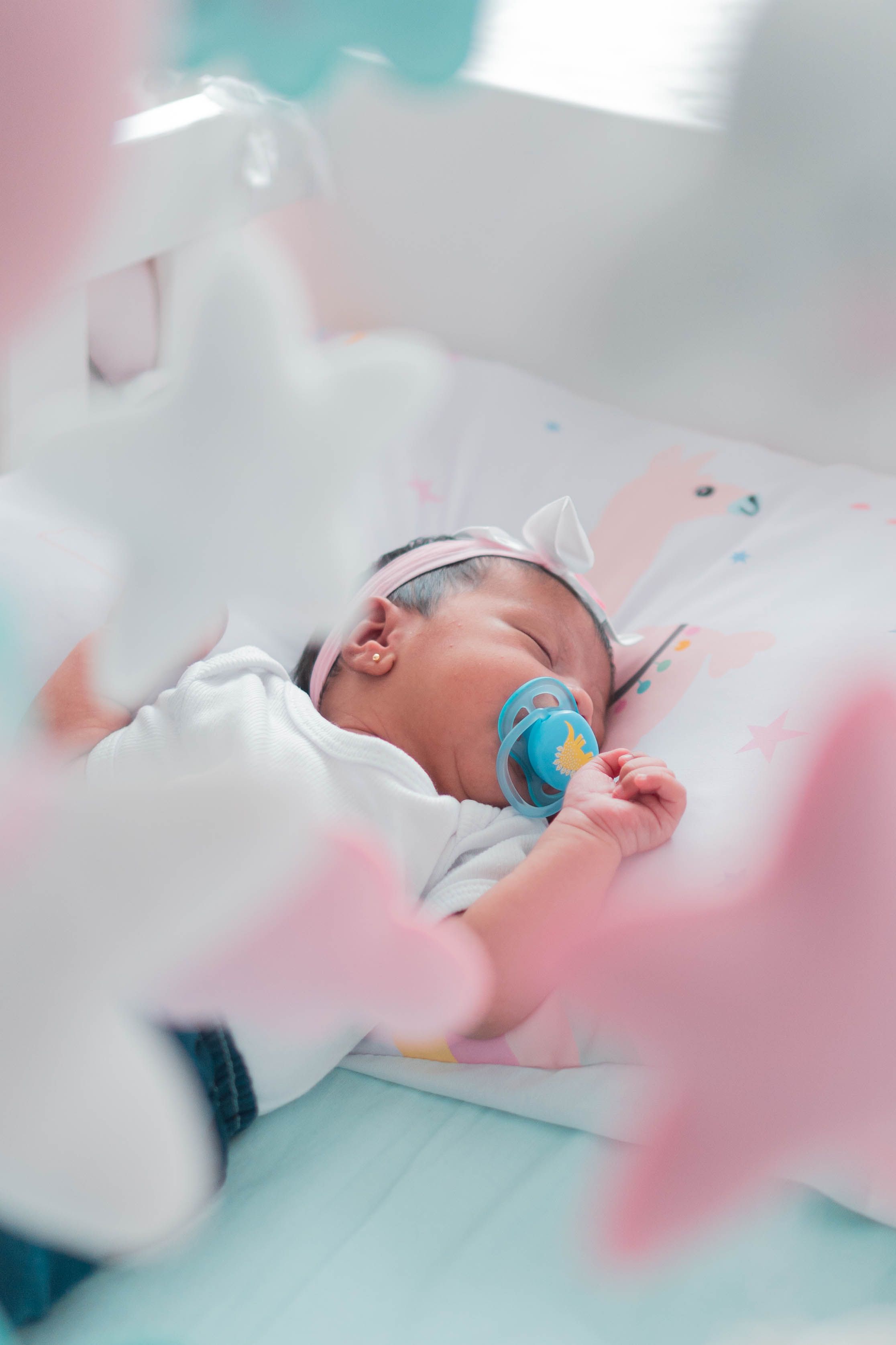 A serene baby sleeping with a pacifier and headband, surrounded by pastel decorations.