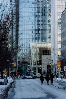 Urban winter scene featuring modern glass facades and people walking on a snowy city street.