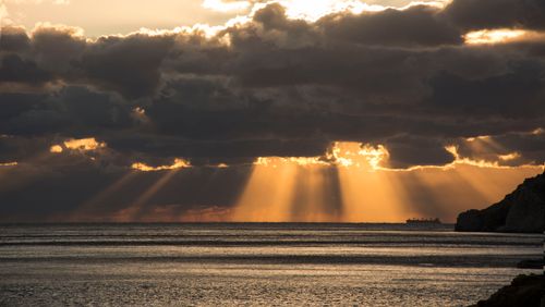 Free Golden sunset illuminating the ocean with striking sunrays through dark clouds, creates dramatic seascape. Stock Photo