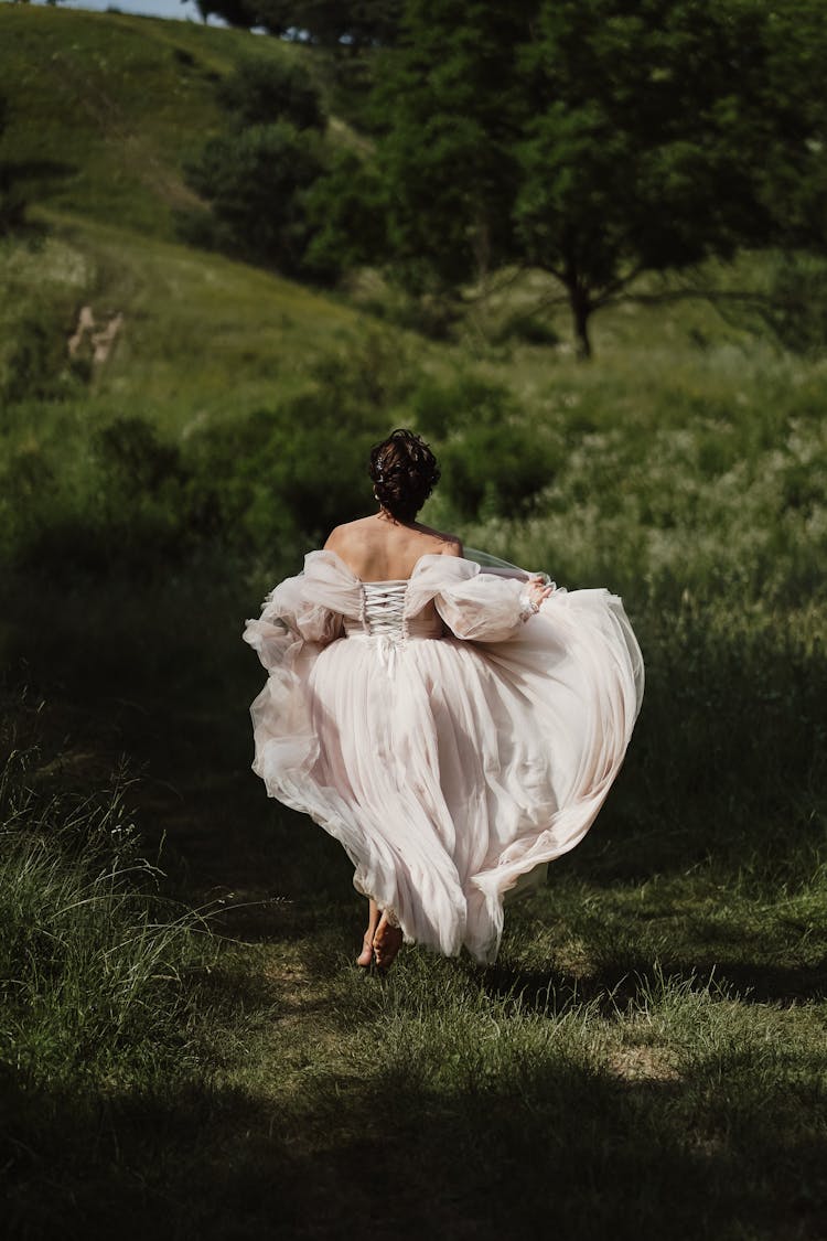 A Woman Wearing White Gown Running On The Grass Field