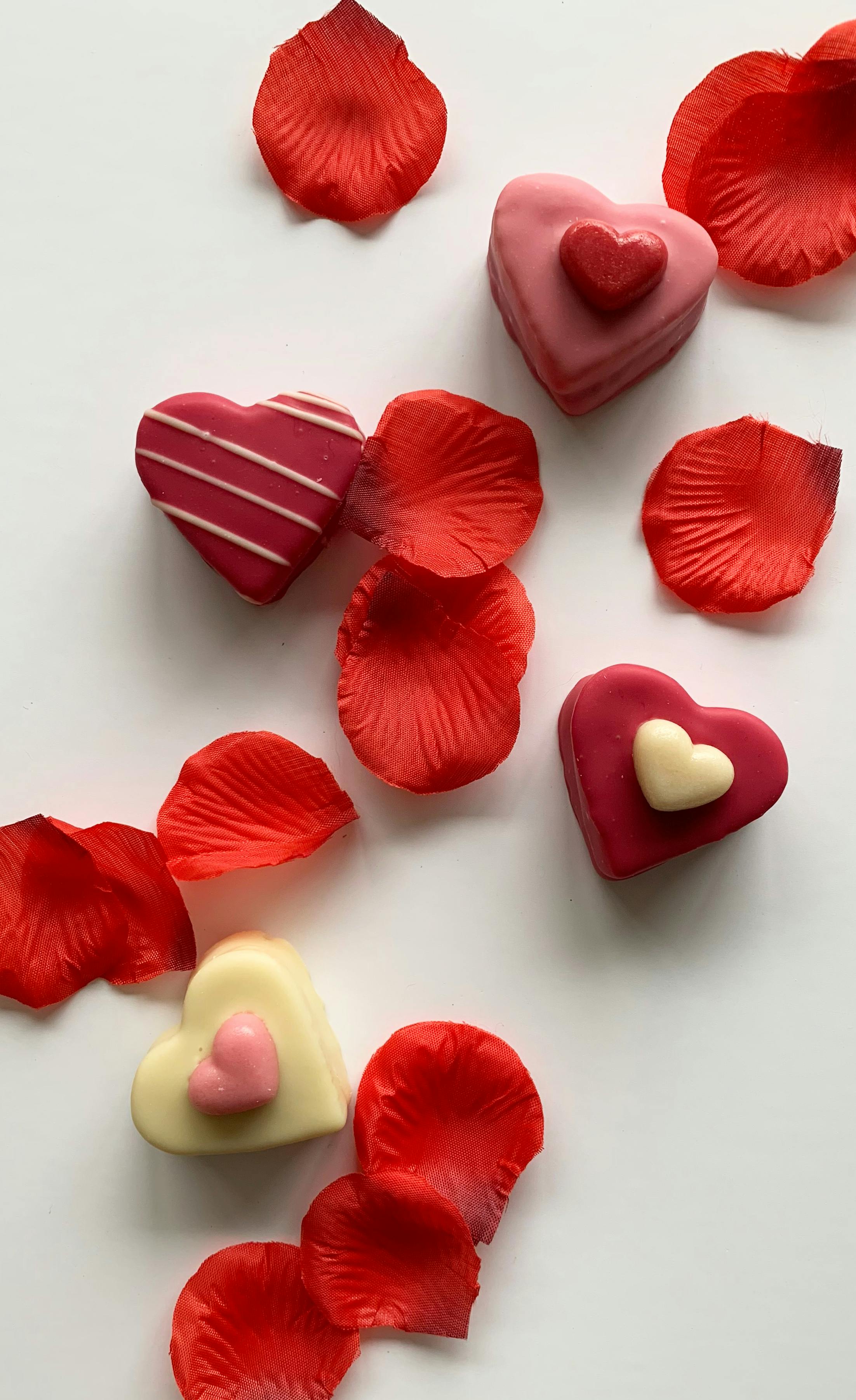 red white and pink sweet cupcakes on white background with rose petals