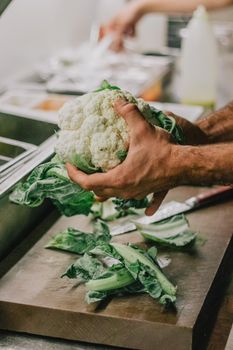 Close-up of hands preparing fresh cauliflower on a cutting board in a kitchen setting.