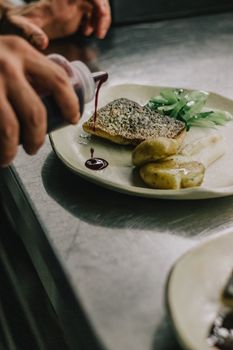 A chef meticulously adds sauce to a gourmet dish, showcasing haute cuisine artistry.