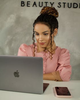 Young woman in a pink dress using a laptop at a beauty studio. Professional work environment.