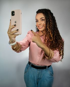 Cheerful young woman in pink top taking a selfie with smartphone.