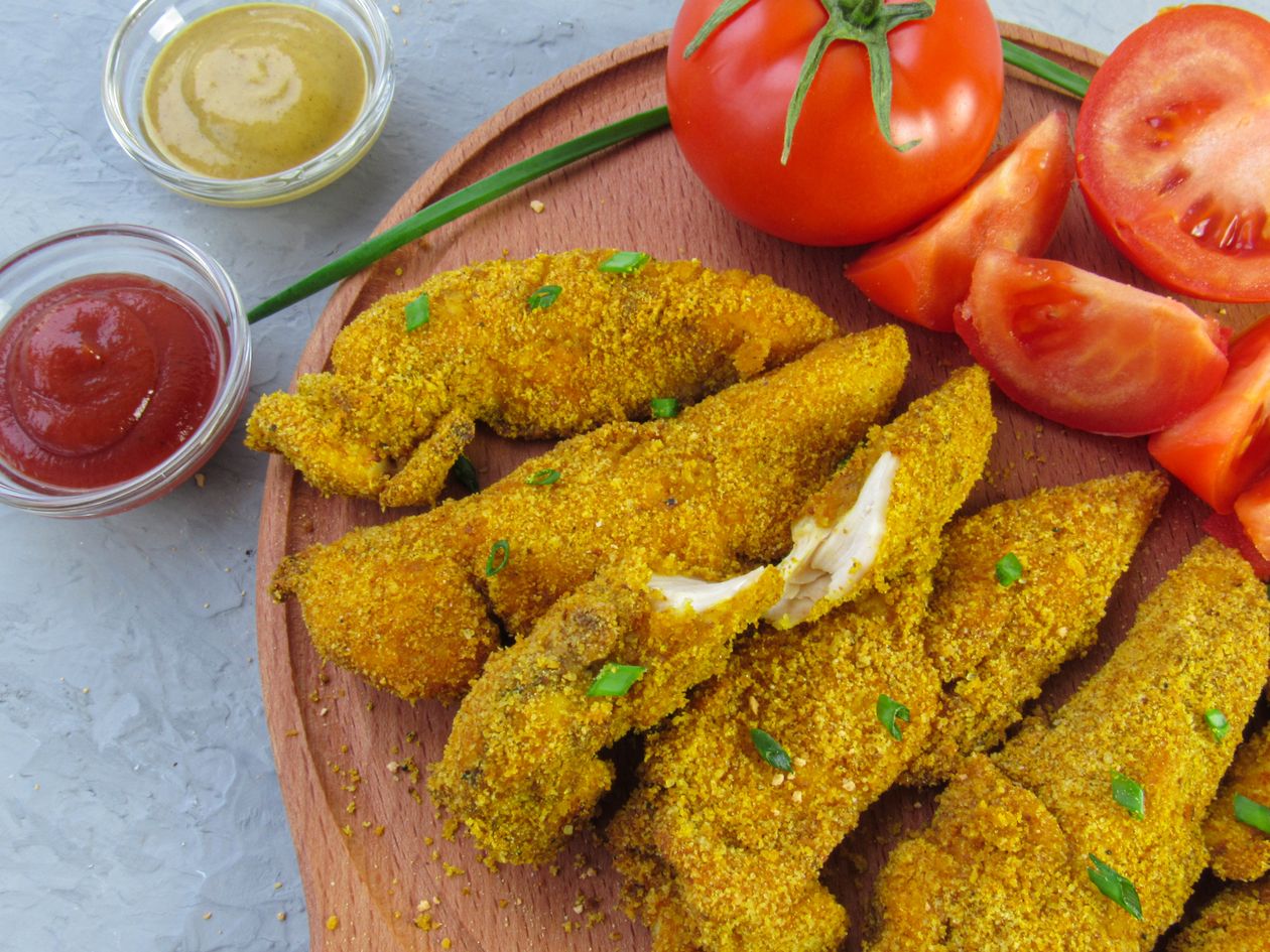 Raw chicken breast tenderloins and sliced chicken thigh pieces laid out next to a marinade bowl and meat mallet on a cutting board
