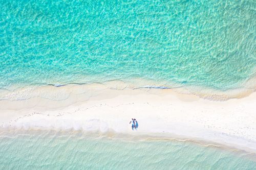Free Aerial shot of a couple lying on a pristine beach with turquoise sea. Stock Photo