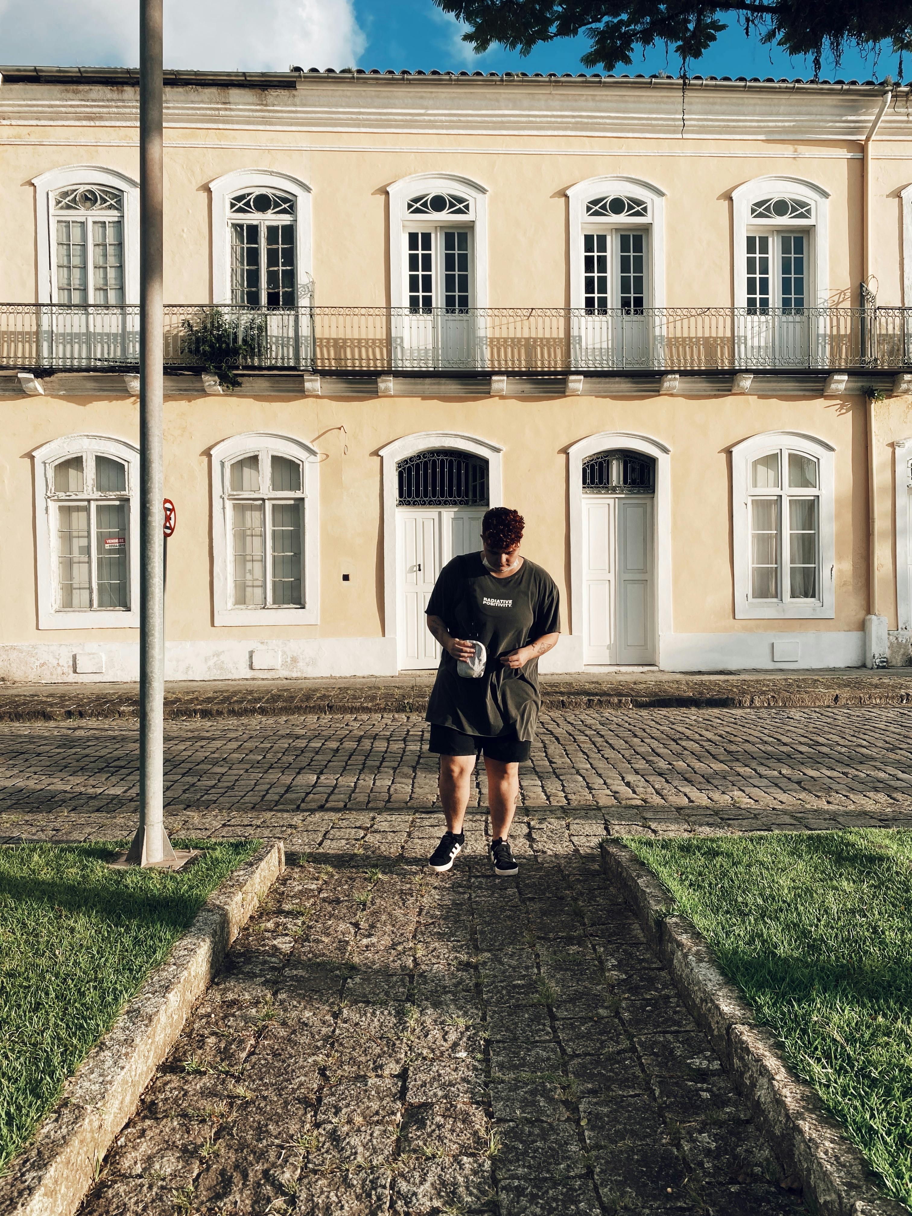 Young man in casual attire stands on cobblestone path outside a historic building facade.