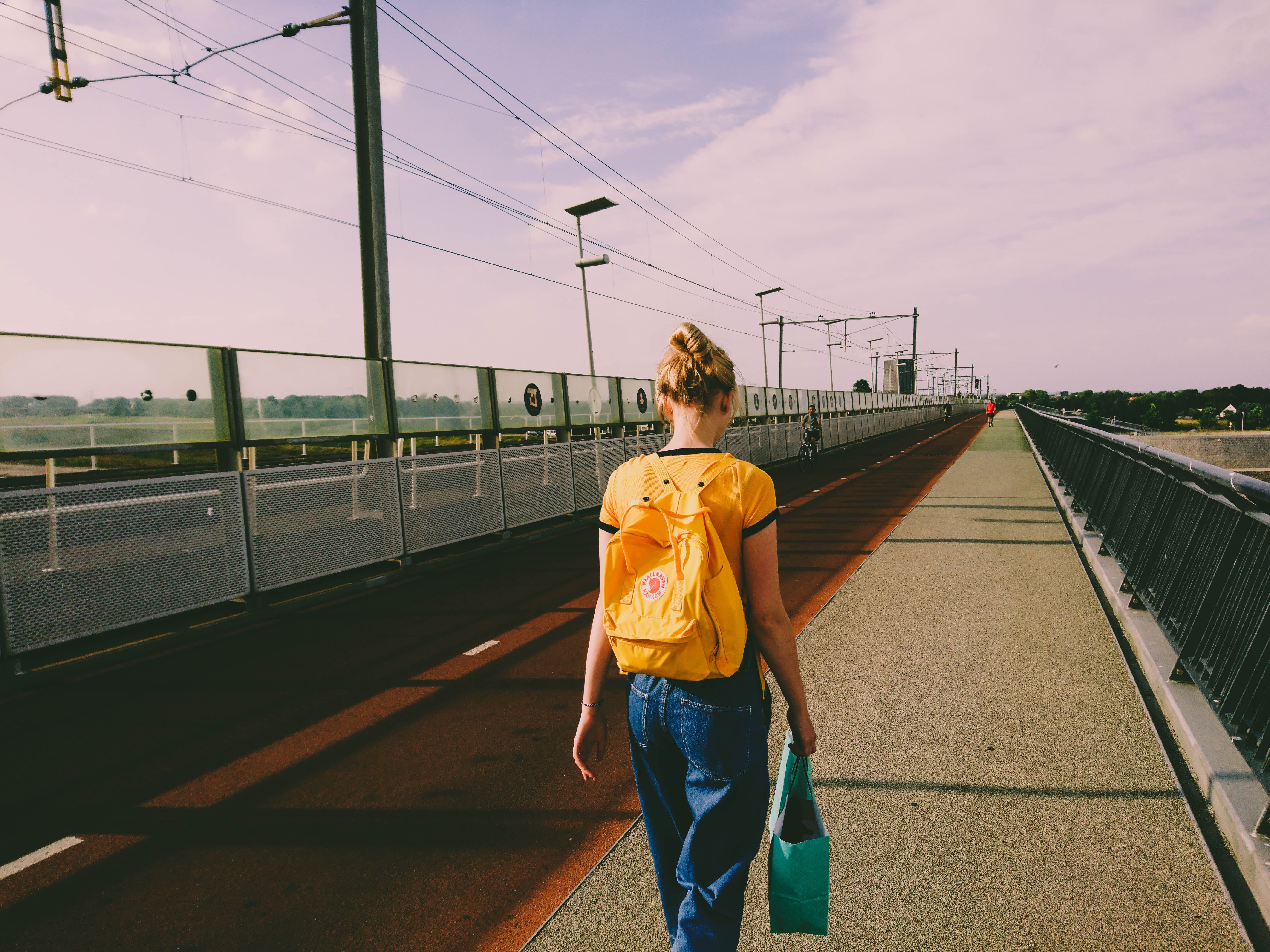 A woman with a yellow backpack walking across a bridge in Nijmegen, Netherlands.