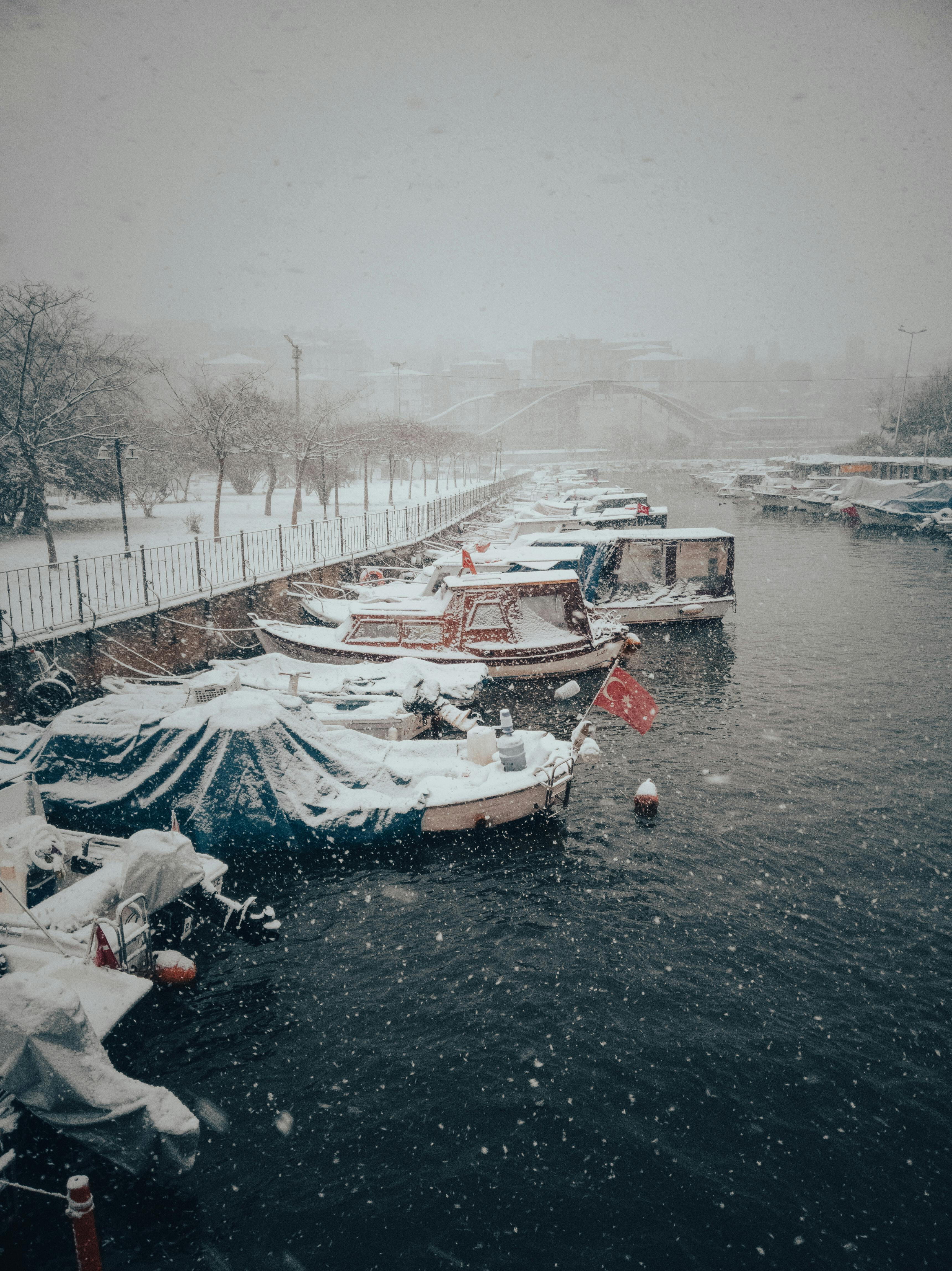 A picturesque winter view of snow-covered boats docked in an Istanbul canal as snowfall blankets the scene.