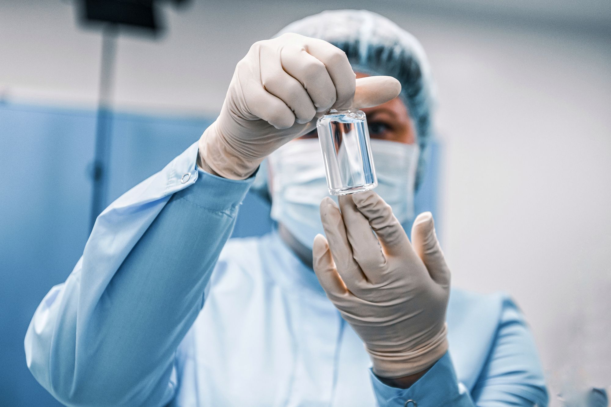 Close-up of a healthcare worker in protective gear examining a medical vial.