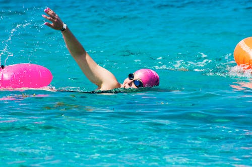 A Woman Wearing Goggles and Swimming Cap While Swimming in a Pool