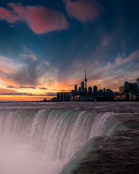 A stunning view of Toronto's skyline against a vibrant sunset with a waterfall in the foreground.