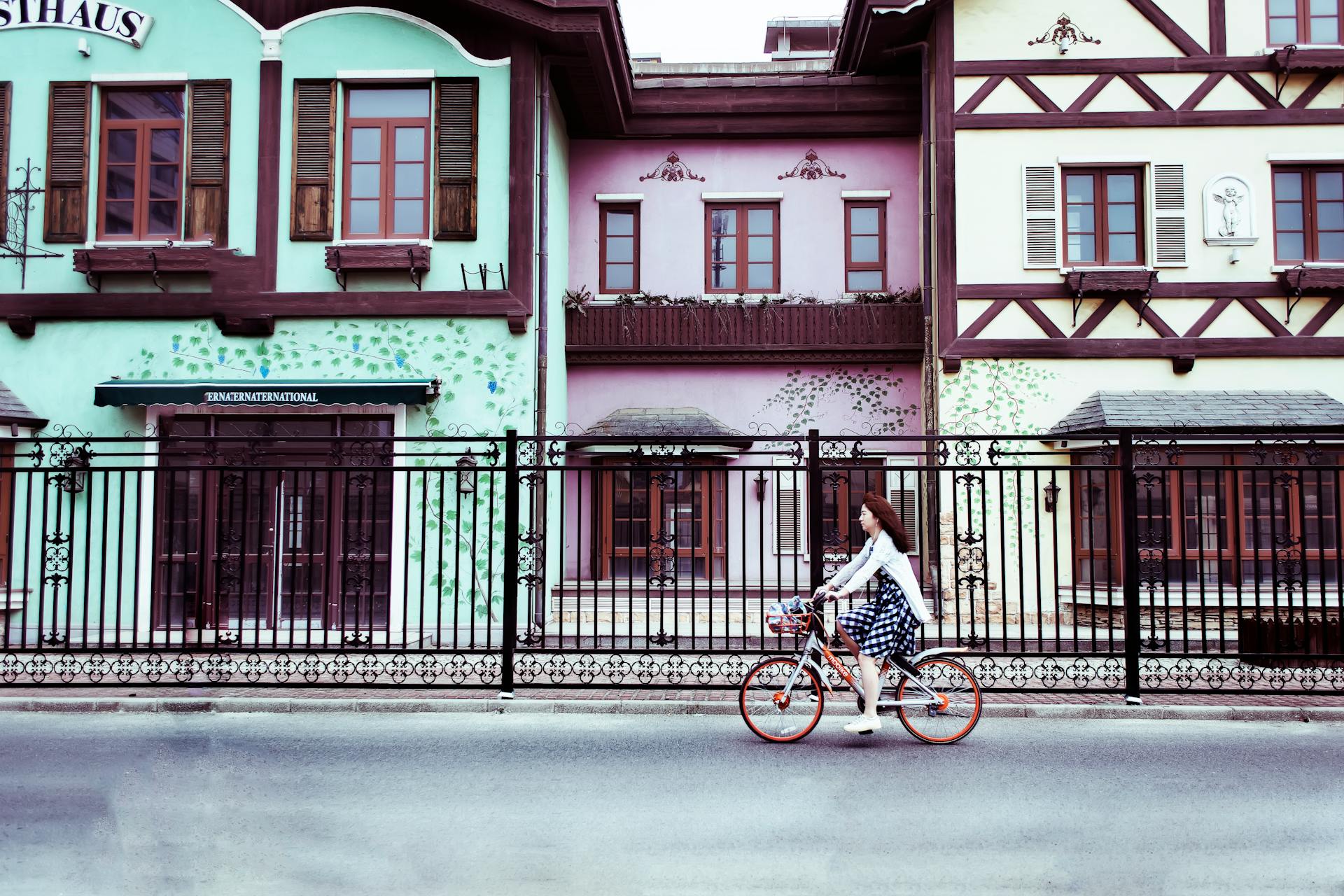 A woman rides a bicycle past colorful European-style houses in an urban setting.