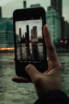 Hand holding smartphone taking a photo of New York City skyline across the river.