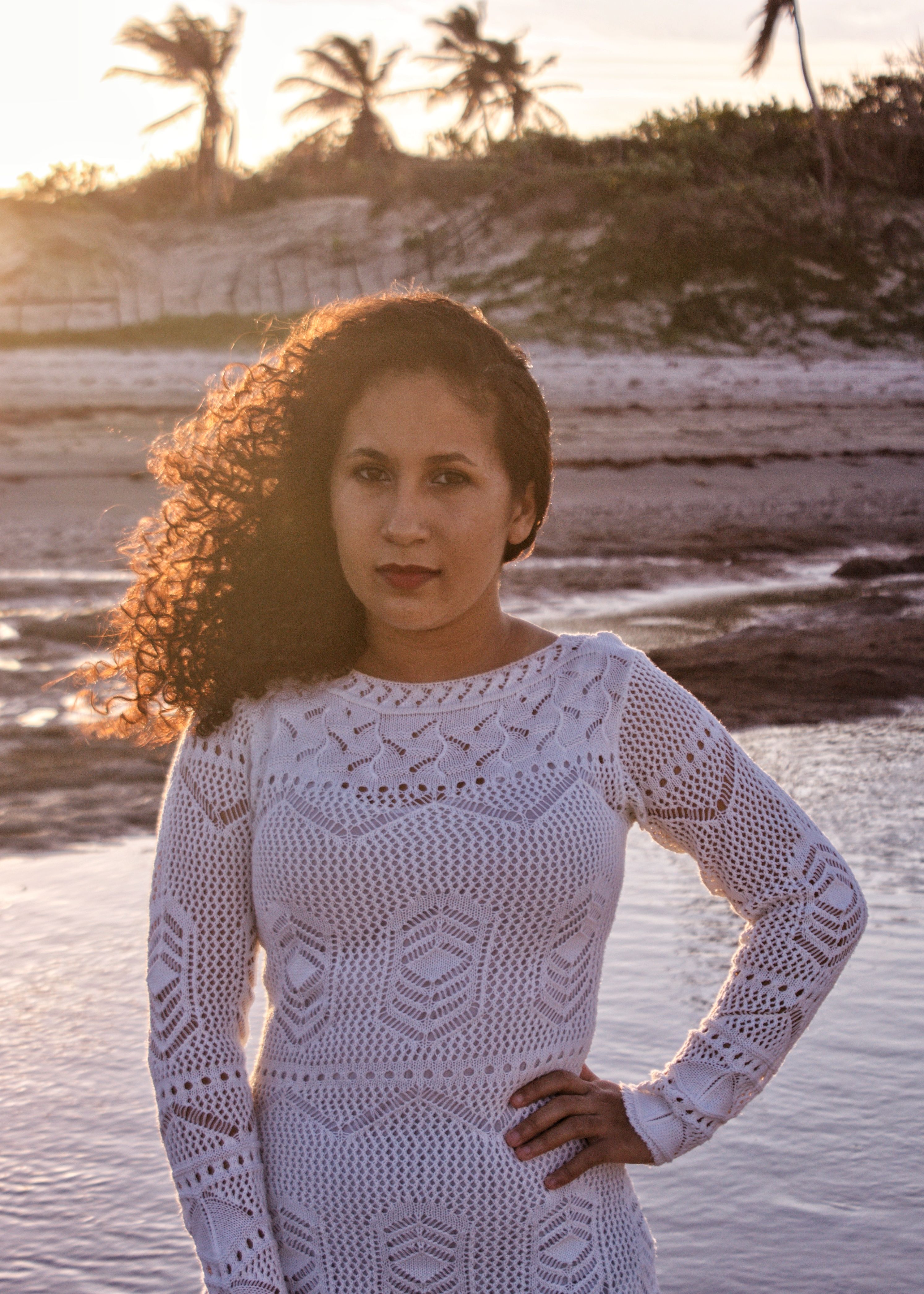 Woman in a white dress standing by the beach at sunset, showcasing natural beauty and tranquility.