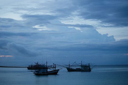 Free Peaceful scene of fishing boats on calm waters under a cloudy evening sky. Stock Photo