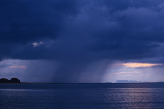 A breathtaking view of rain clouds looming above the calm ocean during twilight, creating a serene seascape.