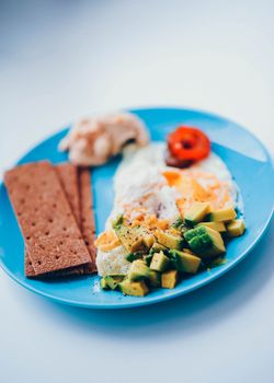 A delectable breakfast plate featuring fried eggs, sliced avocado, and crispy bread crackers.