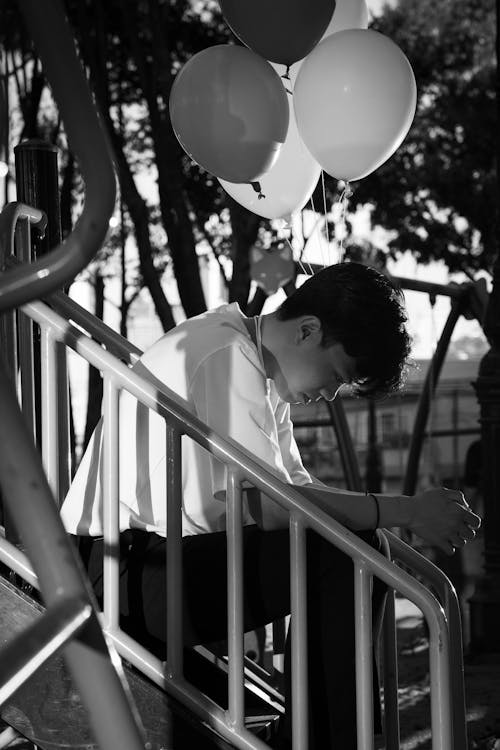 Black and White Photo of a Man Sitting on the Stairs near the Balloons
