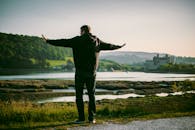 一个人站在河边，伸着双臂欣赏日落美景