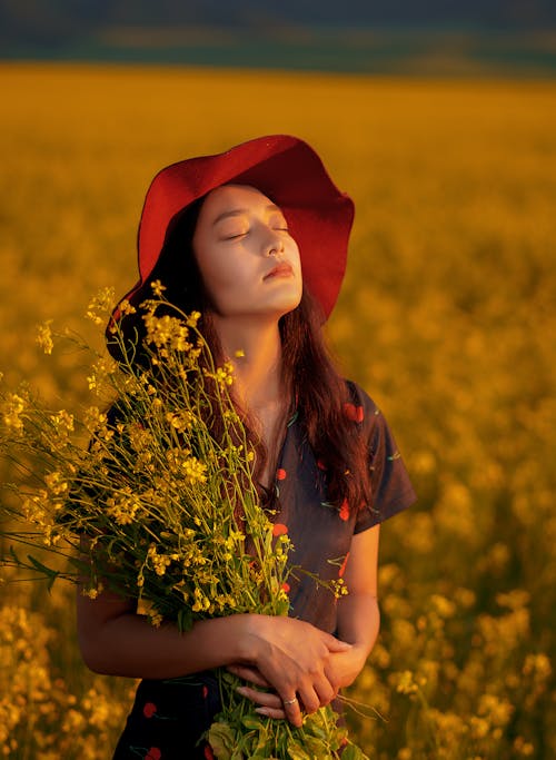 Young Woman in Red Hat Standing in Meadow of Yellow Blossom