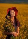 Young Woman in Red Hat Standing in Meadow of Yellow Blossom