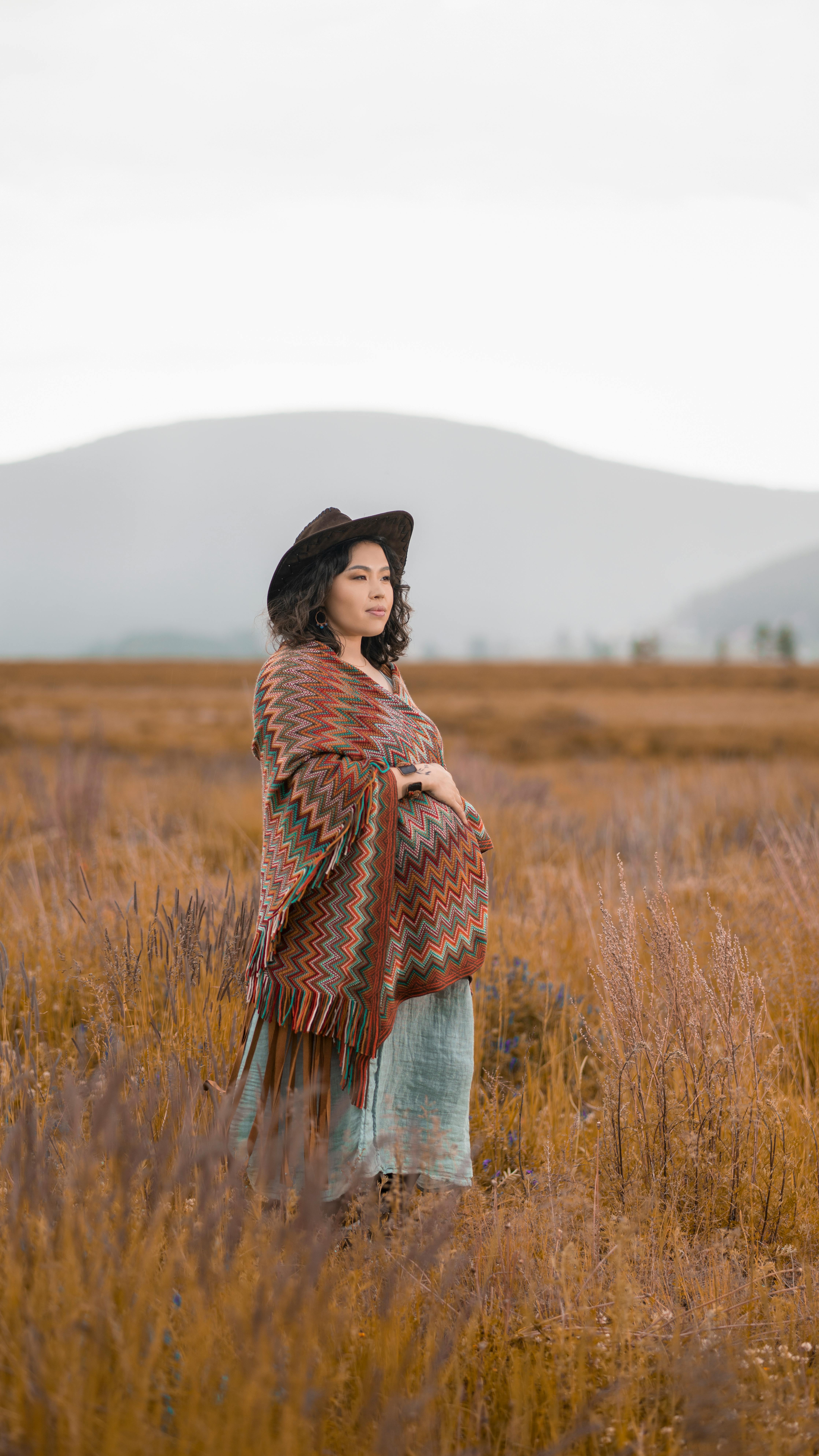 pregnant woman in hat and shawl standing in fields