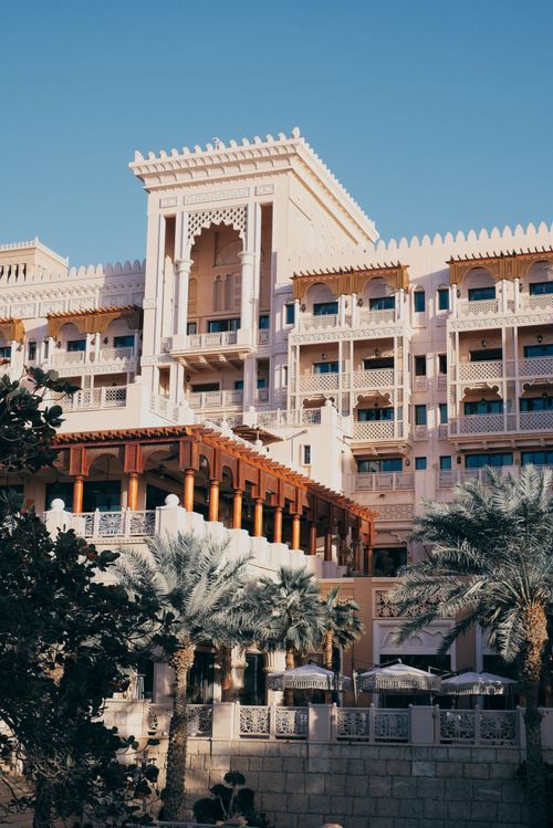 Free Elegant Arabic architectural facade of a luxurious hotel in Dubai, framed by palm trees under a clear blue sky. Stock Photo