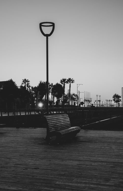 Free A black and white photo of a wooden bench on a coastal walkway at dusk, empty and serene. Stock Photo