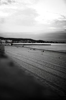 A tranquil monochrome beach scene captured in İzmir, Türkiye, showing the shoreline and distant cityscape.