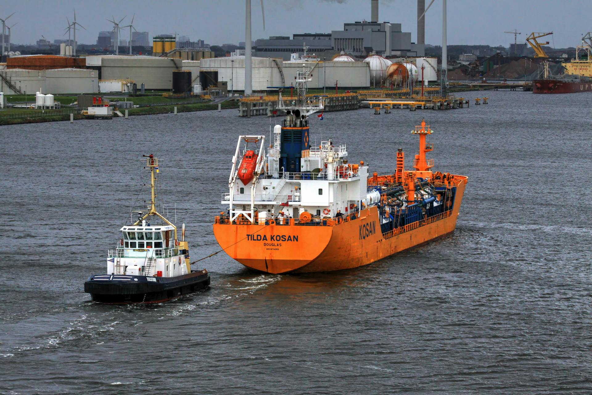 Tugboat towing a cargo ship in the bustling port of Amsterdam, showcasing industrial marine activity.