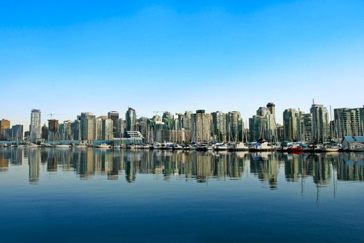 Vancouver skyline with a serene marina reflection under a clear blue sky.