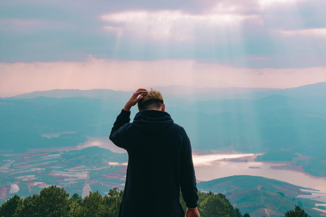 Man in Black Jacket Holding His Hair Facing Body of Water