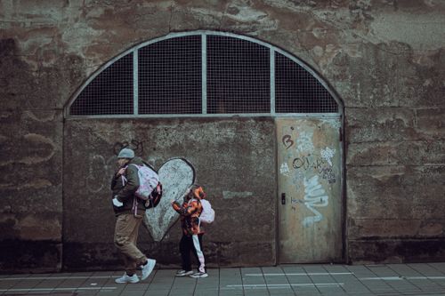 Free A man and child carrying backpacks walk past a graffiti-covered wall outdoors. Stock Photo