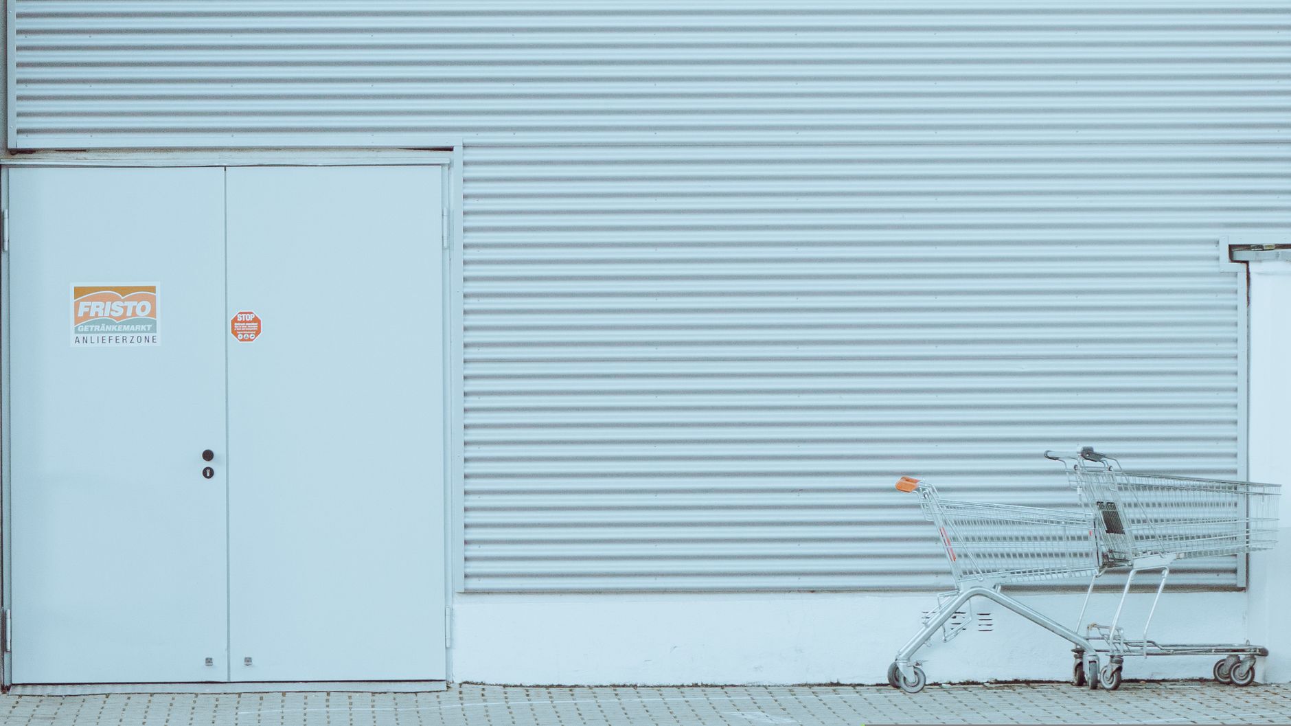A minimalist urban setting featuring a turquoise corrugated wall and an empty shopping cart.